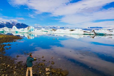 Adam muhteşem manzaranın fotoğrafını çekiyor. İzlanda. Beyaz ve mavi buzdağları ve buz kütleleri Jokulsaurlounda yansıyor. Ekstrem, kuzey ve fotoğraf turizmi kavramı.