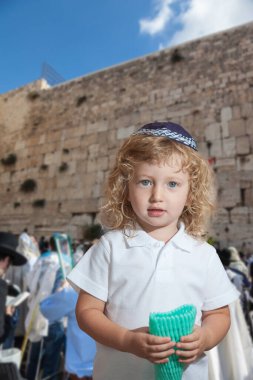 Autumn Jewish holiday Sukkot. The greatest shrine of Judaism is the Western Wall of the Temple. Lovely blonde boy with blue eyes in a skullcap clipart