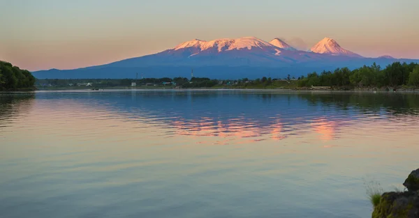 Solnedgång belysning Kluchevskaja grupp av vulkaner med reflektion i floden Kamchatka. — Stockfoto
