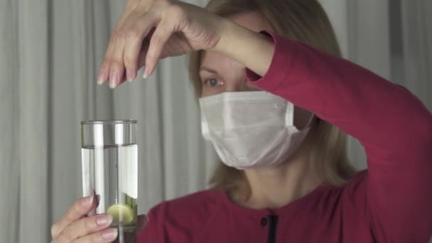 Femme malade dans le masque médical dissout la tablette effervescente dans un verre d'eau au ralenti stock de séquences vidéo — Video