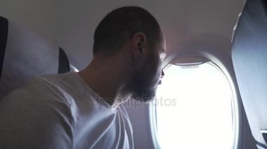 Uçak uçan ve müzik kulaklık smartphone ile pencere yanında oturan adam. stok görüntüleri video