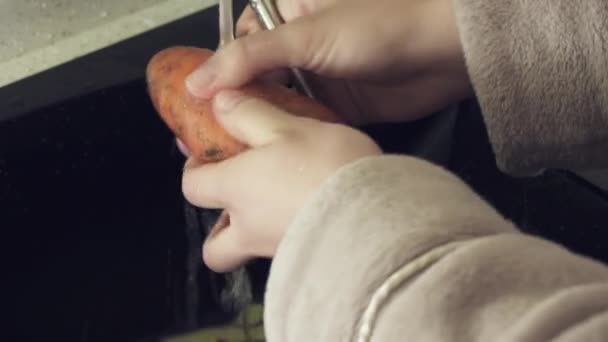 Housewife cleans carrots under running water in kitchen stock footage video — Stock Video