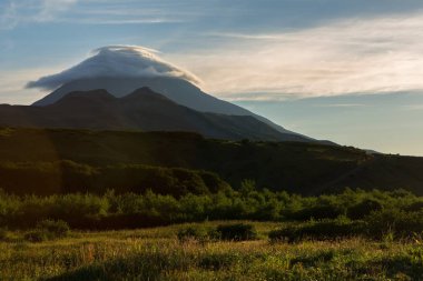 Lenticular clouds above Vilyuchinsky stratovolcano at dawn. View from brookvalley Spokoyny at the foot of outer north-eastern slope of caldera volcano Gorely. clipart