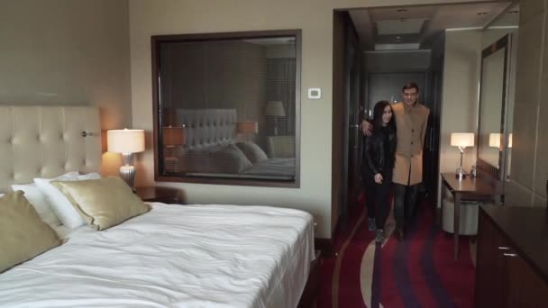Casal apaixonado entra no quarto com mala e alegremente cai na cama de câmera lenta de imagens de vídeo — Vídeo de Stock