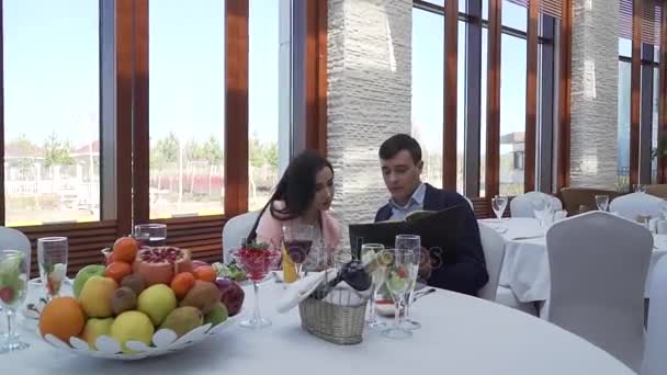 Guy avec une fille dans un restaurant à table explorant le menu stock vidéo — Video
