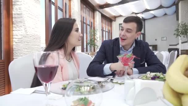 Pareja en el amor en la cena del restaurante, chico alimenta a una chica con una baya en un beso de archivo de vídeo — Vídeos de Stock