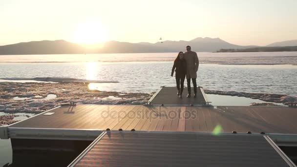 Bevroren maar gelukkig verliefde paar wandelingen op pier bij zonsondergang stock footage video — Stockvideo