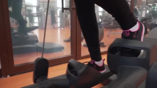 Молодая девушка тренируется на тренера по эллипсу в тренажерном зале — стоковое видео