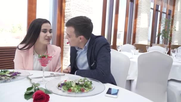 Pareja en el amor en la cena del restaurante, chico alimenta a una chica con una baya en un beso cámara lenta archivo de vídeo — Vídeos de Stock