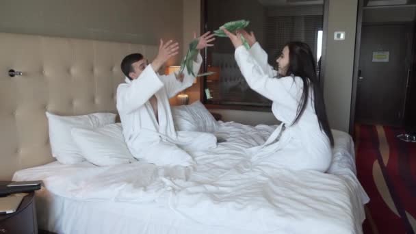 Amante casal em casacos brancos na cama alegremente vomita dinheiro, grandes ganhos vídeo de imagens de estoque de câmera lenta — Vídeo de Stock