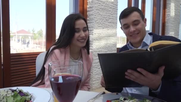 Mann mit einem Mädchen in einem Restaurant am Tisch, das die Speisekarte in Zeitlupe betrachtet — Stockvideo