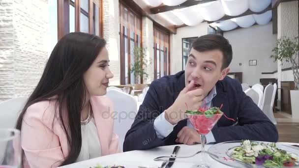 Пара влюблённых за ужином в ресторане, парень кормит девушку ягодами в видеозаписи поцелуев — стоковое видео