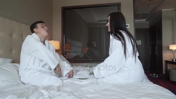 Любящая пара в белых халатах на кровати радостно выбрасывает наличные, большой выигрыш замедленной съемки акции видео — стоковое видео