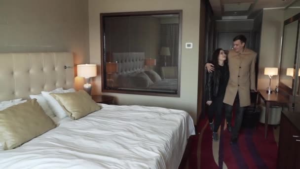 Para w miłość przychodzi do pokoju z walizką i radośnie przypada na łóżku zwolnionym tempie czas nagrania wideo — Wideo stockowe