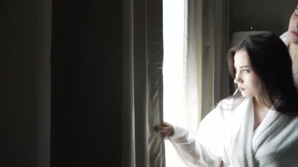 Αγαπώντας ζευγάρι σε λευκό παλτό εξετάζει το τοπίο έξω από το παράθυρο και φιλιά Χρηματιστήριο πλάνα βίντεο — Αρχείο Βίντεο