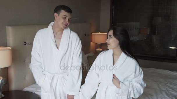 Amante casal em casacos brancos felizmente pula na cama de câmera lenta imagens de vídeo — Vídeo de Stock