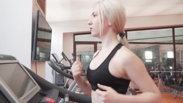Chica joven entrena en una cinta de correr en el gimnasio material de archivo de vídeo — Vídeo de stock
