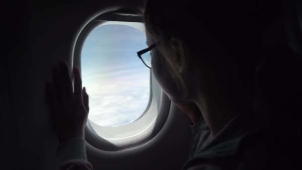 Jovem com óculos olha com interesse para a janela de um filme de estoque de avião vídeo — Vídeo de Stock