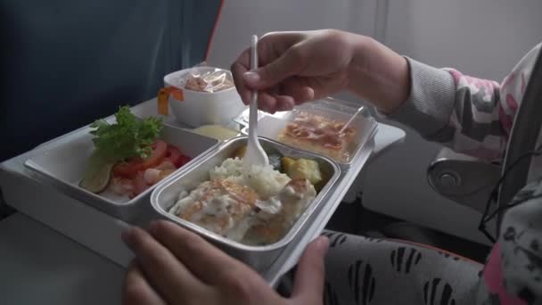 Chica joven en los auriculares está comiendo deliciosa cena en el video de archivo de avión — Vídeos de Stock