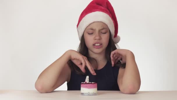 Menina adolescente feliz bonita em um chapéu de Papai Noel sonha com um presente, recebe vários presentes desnecessários e expressa prazer apenas para o cão doado no fundo branco imagens de vídeo — Vídeo de Stock