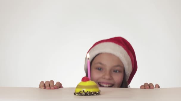 Belle fille coquine adolescente dans le chapeau du Père Noël souffle secrètement bougie sur gâteau festif sur fond blanc vidéo de fond — Video