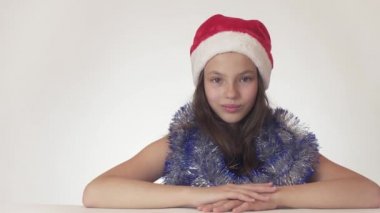 Güzel genç kız Santa Claus şapka ve oturma ve bir hediye, rüya yeni yıl tinsel ifade utanç ve çekicilik üzerinde beyaz arka plan stok görüntüleri video