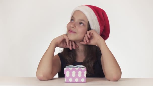 Menina adolescente feliz bonita em um chapéu de Papai Noel sonhos de um presente, recebe presente em uma caixa, joga fora um presente de antipatia e sonhos de outro em fundo branco imagens de vídeo — Vídeo de Stock