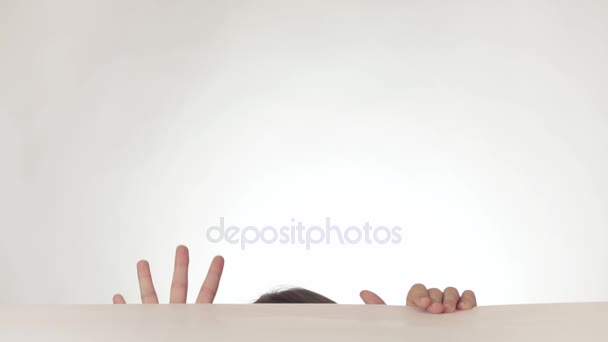 Beautiful happy naughty teen girl having fun getting out from under the table and hiding back on white background stock footage video. — Stock Video