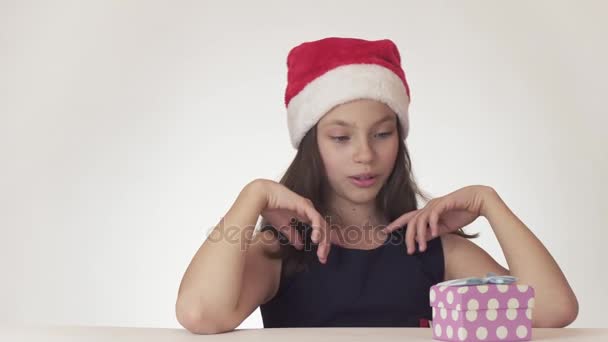 Mooie tiener meisje in een kerstman hoed dromen van een geschenk, ontvangt de gewenste geschenk en is erg blij op witte achtergrond stock footage video — Stockvideo