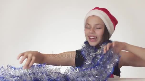Schönes Teenie-Mädchen mit Weihnachtsmann-Hut und Silvesterlametta tanzt fröhlich und verschmitzt auf weißem Hintergrund — Stockvideo
