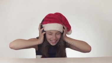 Güzel yaramaz kız genç bir Noel Baba şapkalı kulaklıklar müzik dinler ve boyunca üzerinde beyaz arka plan stok görüntüleri video şarkı söylüyor.