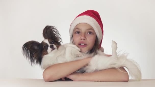 サンタ クロースの帽子の美しい 10 代の少女は喜んで白い背景ストック映像ビデオの彼女の犬を抱擁します。 — ストック動画