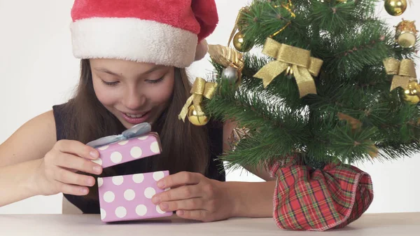 Vacker stygg flicka Tonåring i en jultomten hatt i hemlighet tittar gåva under nyår träd på vit bakgrund — Stockfoto
