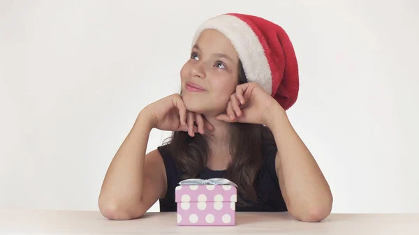 Belle jeune fille dans le chapeau du Père Noël assis et fait un souhait sur fond blanc — Photo