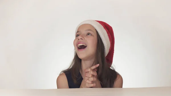 Bella ragazza felice adolescente in un look cappello di Babbo Natale ed esprime emotivamente una sorpresa su sfondo bianco — Foto Stock