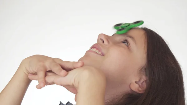 Bela menina adolescente alegre girando um fidget spinner verde em sua testa no fundo branco — Fotografia de Stock