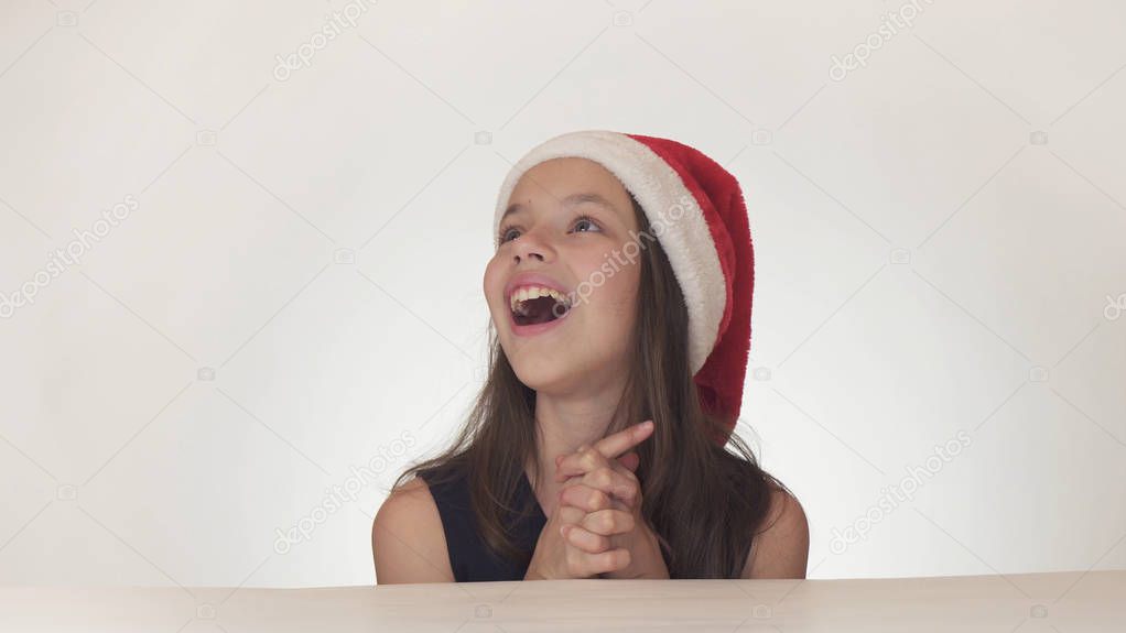 Beautiful happy girl teenager in a Santa Claus hat look and emotionally expresses a surprise on white background