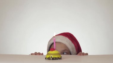 Noel Baba şapkalı güzel yaramaz kız genç gizlice dışarı şenlikli pasta beyaz arka plan stok görüntüleri video üzerinde mum darbeler.