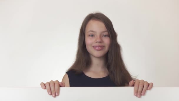Hermosa chica adolescente sostiene un póster con información y alegremente lo anuncia en el video de archivo de fondo blanco . — Vídeo de stock