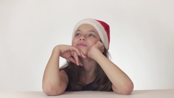 Linda menina feliz adolescente em um chapéu de Papai Noel sonha alegremente e ri no fundo branco imagens de vídeo . — Vídeo de Stock