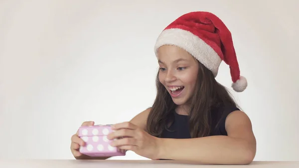 Hermosa chica adolescente en un sombrero de Santa Claus está satisfecho con el regalo en la caja sobre fondo blanco —  Fotos de Stock