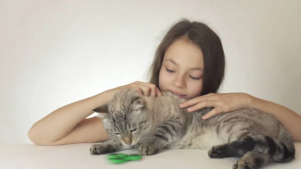 Веселая девочка-подросток с котом, играющим с зеленым фиолетовым спиннером на белом фоне — стоковое фото