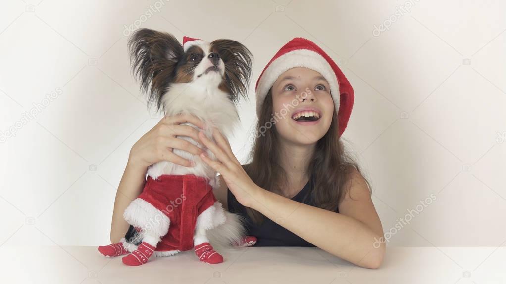 Beautiful teen girl and dog Continental Toy Spaniel Papillon in Santa Claus costumes joyfully looking around and laughing on white background
