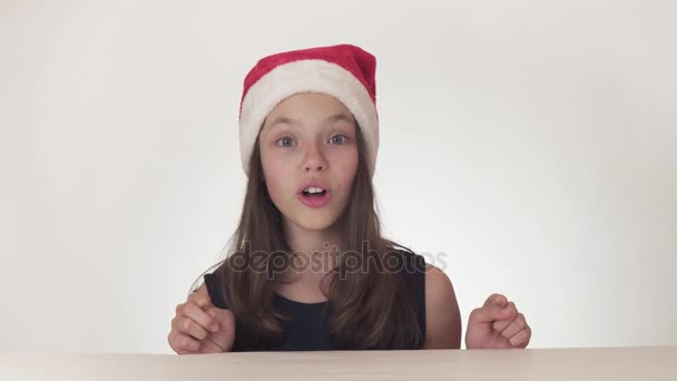 Hermosa chica feliz adolescente en un sombrero de Santa Claus expresa emocionalmente una alegre sorpresa en el fondo blanco de archivo de vídeo . — Vídeos de Stock