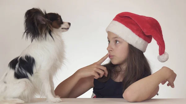 Όμορφο εφηβικό κορίτσι στον Αϊ Βασίλη καπέλο ευτυχώς συναισθηματικά επικοινωνεί με το σκύλο σε λευκό φόντο — Φωτογραφία Αρχείου