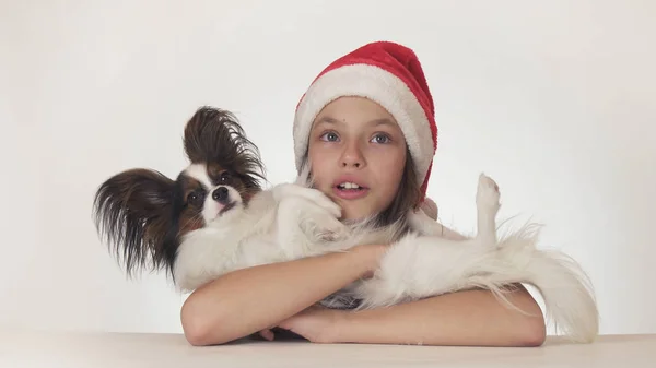 Hermosa adolescente en Santa Claus sombrero felizmente abraza a su perro y se ven sorprendidos en el fondo blanco —  Fotos de Stock