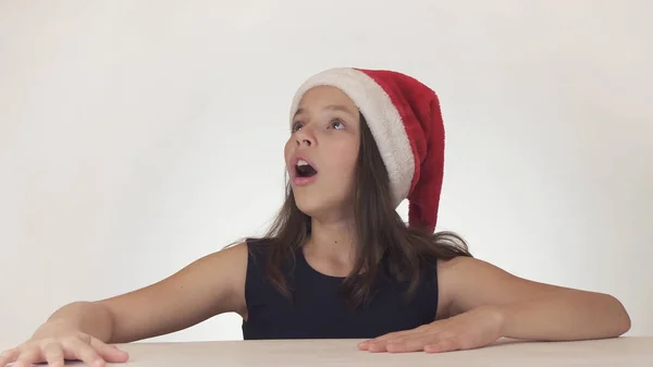 Menina feliz bonita adolescente em um olhar de chapéu de Papai Noel e emocionalmente expressa uma surpresa no fundo branco — Fotografia de Stock