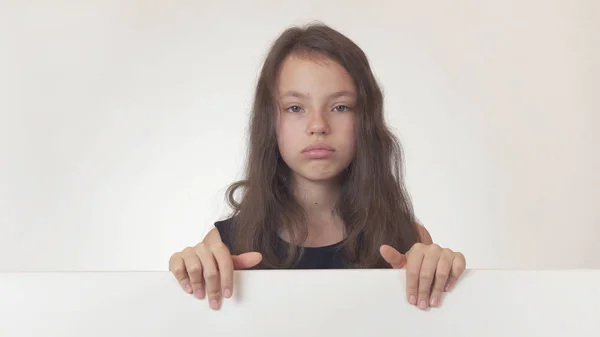 Menina bonita adolescente segurando um pôster com informações e expressando decepção e tristeza no fundo branco — Fotografia de Stock