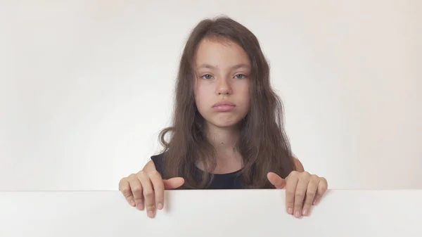 Beautiful girl teenager holding a poster with information and expressing disappointment and sadness on white background — Stock Photo, Image