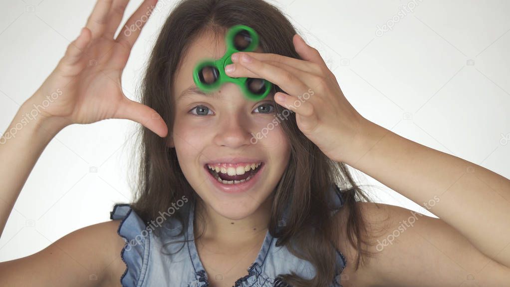 Beautiful cheerful teen girl playing with green fidget spinner on white background